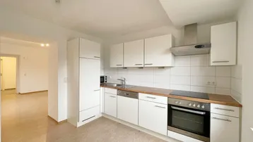Helle Einbauküche mit weißen Schränken, Holz-Arbeitsplatte und Blick in den angrenzenden Wohnbereich.