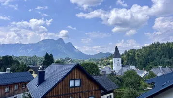 Malerischer Ausblick auf ein Dorf mit Kirche und majestätischen Bergen unter blauem Himmel.