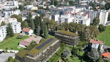 Moderne Wohngebäude mit Gründächern und Photovoltaikanlagen in einer grünen Wohngegend mit Bergblick.