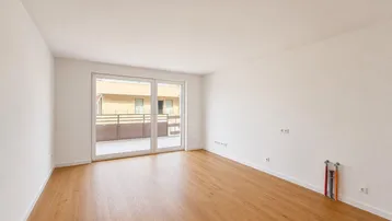 Helles, leeres Zimmer mit Holzboden und Zugang zu einem Balkon, bereit für die Einrichtung.