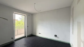 Unfertiger Raum mit sichtbarer Fußbodenheizung und Zugang zu einem Balkon, bereit für den Ausbau.