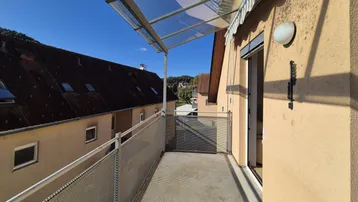 Heller Balkon mit Glasüberdachung und Metallgeländer, bietet einen Blick auf die Umgebung.
