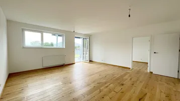 Helles Wohnzimmer mit Holzboden, weißen Wänden und Zugang zu einem Balkon oder einer Terrasse.