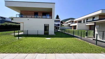 Weitläufige Ansicht der modernen Wohngebäude mit grünen Gärten und hügeliger Landschaft im Hintergrund.