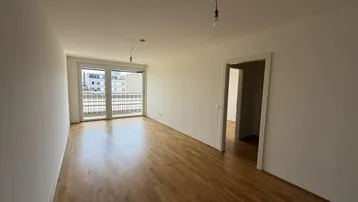 Helles, leeres Wohnzimmer mit Holzboden und Zugang zu einem Balkon, bereit zur Einrichtung.