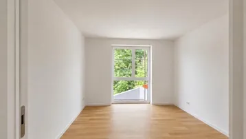 Helles, leeres Zimmer mit Holzboden und Blick ins Grüne durch das Fenster.