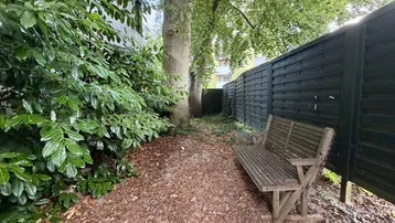Ruhiger Gartenbereich mit einer Holzbank und einem Sichtschutzzaun.