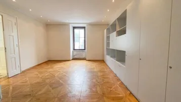 Heller Wohnraum mit elegantem Parkettboden, integrierten weißen Schränken und einem Fenster für natürliches Licht.