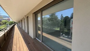 Langer, moderner Balkon mit Holzboden und großen Schiebetüren, bietet viel Tageslicht und Ausblick.