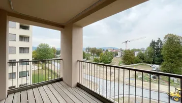 Geräumiger Balkon mit Holzdielenboden und Blick auf die umliegende Bebauung und eine Baustelle.