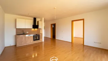 Geräumiger Wohnbereich mit integrierter Küchenzeile und hellem Laminatboden.