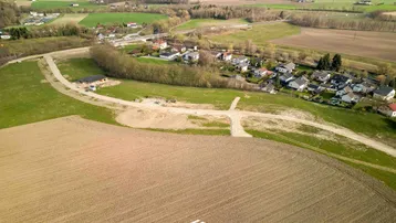 Luftaufnahme eines ländlichen Baugebiets mit Feldern, Wiesen und einigen Häusern in der Ferne.