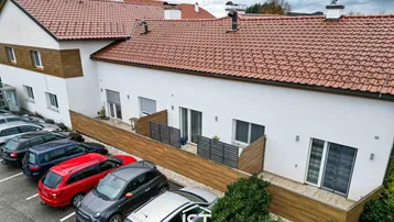 Außenansicht eines modernen Wohngebäudes mit Parkplätzen und Terrassen im Erdgeschoss.