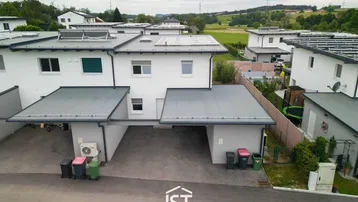 Moderne Reihenhäuser mit Carports und Photovoltaikanlagen in ländlicher Umgebung.