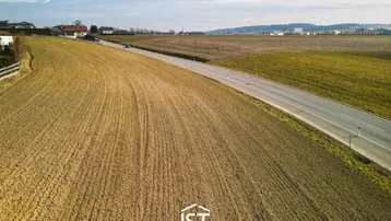 Luftaufnahme eines weiten Feldes neben einer Landstraße mit ländlicher Bebauung im Hintergrund.