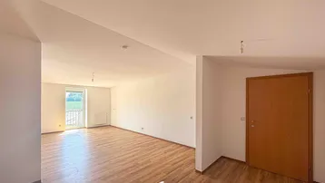 Helles, leeres Wohnzimmer mit Laminatboden und Zugang zu einem kleinen Balkon.