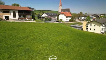 Grünes Baugrundstück in ländlicher Umgebung mit Blick auf die Kirche und umliegende Häuser.