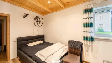 Gemütliches Schlafzimmer mit Holzbalkendecke, Doppelbett und Fenster mit Blick ins Grüne.