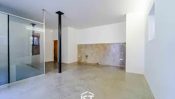 Heller Raum mit Betonboden, weißen Wänden und vorbereiteten Anschlüssen für eine Küche.
