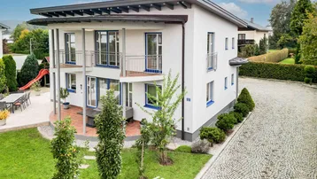 Modernes Wohnhaus mit mehreren Balkonen, gepflegtem Vorgarten und gepflasterter Auffahrt.
