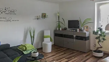 Helles Wohnzimmer mit Holzboden, bequemer Couch und einem Fenster, das Tageslicht hereinlässt.