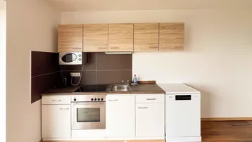 Moderne Einbauküche mit hellen Holzschränken, weißen Unterschränken und integrierten Geräten.