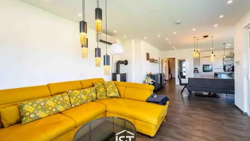 Lichtdurchflutetes Wohnzimmer mit gelbem Ecksofa und gemütlichem Kaminofen.