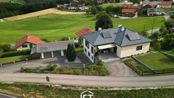 Luftaufnahme eines Einfamilienhauses mit Solaranlage auf dem Dach und ländlicher Umgebung.