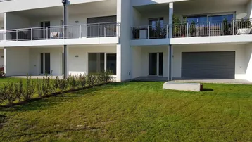 Moderne Wohnanlage mit weißer Fassade, Balkonen und gepflegter Rasenfläche vor dem Gebäude.
