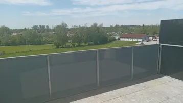 Geräumiger Balkon mit Fliesenboden und weitem Blick über die grüne Landschaft unter blauem Himmel.