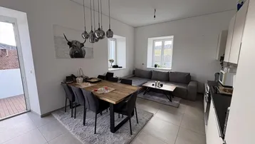Heller, offener Wohn-Essbereich mit moderner Küche, Fliesenboden und Zugang zum Balkon.