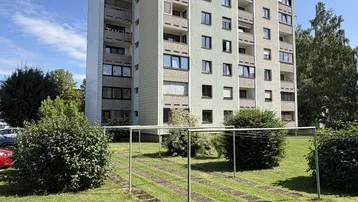 Mehrstöckiges Wohngebäude mit Balkonen und gepflegter Grünfläche im Vordergrund unter blauem Himmel.