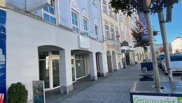 Blick auf die Fassade eines Gebäudes an einer belebten Straße mit Geschäften im Erdgeschoss.