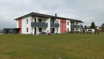 Mehrfamilienhaus mit moderner Fassade, Balkonen und großem Rasenbereich im Vordergrund.