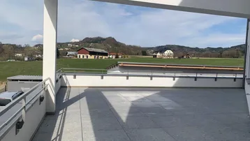 Geräumige, geflieste Terrasse mit Blick auf grüne Felder und die ländliche Umgebung unter blauem Himmel.