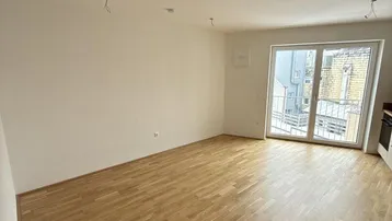 Geräumiger Wohnbereich mit hellem Parkettboden und Zugang zu einem französischen Balkon.