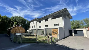 Moderne Wohnanlage mit mehreren Einheiten, kleinem Gartenbereich und Garagen unter blauem Himmel.