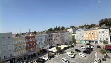Panoramablick über einen belebten Stadtplatz mit parkenden Autos und historischen Gebäuden.