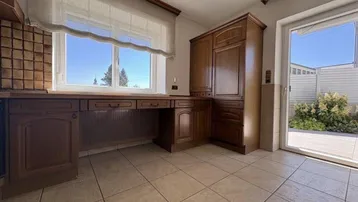 Gemütliche Küche mit Holzmöbeln, Fliesenboden und einem Fenster mit weitem Blick ins Grüne.