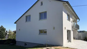 Freistehendes Einfamilienhaus mit weißer Fassade, Satteldach und einem gepflegten Gartenbereich.