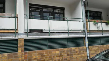 Fassade eines Mehrfamilienhauses mit Balkonen, grünen Geländern und einem geparkten Auto davor.
