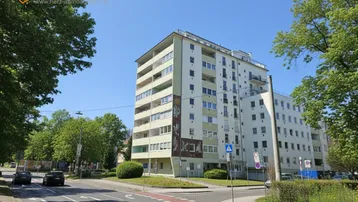 Mehrstöckiges Wohngebäude an einer Straßenecke mit Bäumen und klarem Himmel.