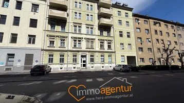 Mehrfamilienhaus mit klassischer Fassade und Balkonen an einer städtischen Straße.