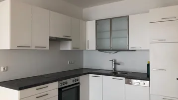 Moderne Einbauküche mit weißen Schränken, dunkler Arbeitsplatte und integrierten Geräten.