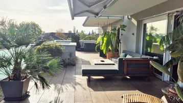Geräumige Dachterrasse mit bequemen Loungemöbeln, vielen Pflanzen und ausfahrbarer Markise.