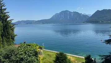 Atemberaubender Panoramablick auf den glitzernden See und die majestätischen Berge unter blauem Himmel.