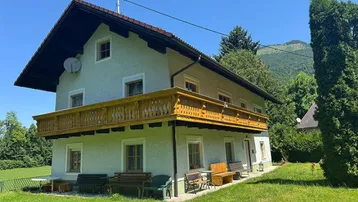 Traditionelles Haus mit Holzbalkon und Bergblick in grüner ländlicher Umgebung.