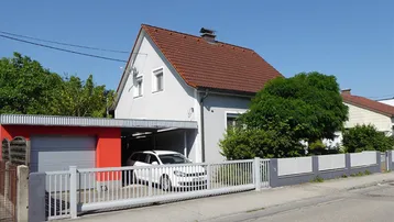 Einfamilienhaus mit Satteldach, Carport und Garage, umgeben von einem gepflegten Zaun.