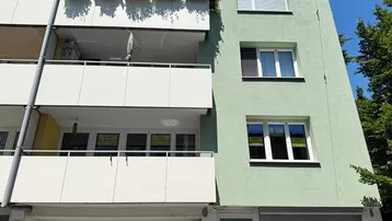 Fassade eines Mehrfamilienhauses mit hellgrünem Putz und mehreren Balkonen unter blauem Himmel.