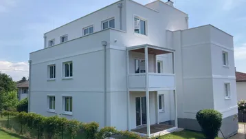 Modernes Mehrfamilienhaus mit weißer Fassade und Balkonen in einer grünen Umgebung.